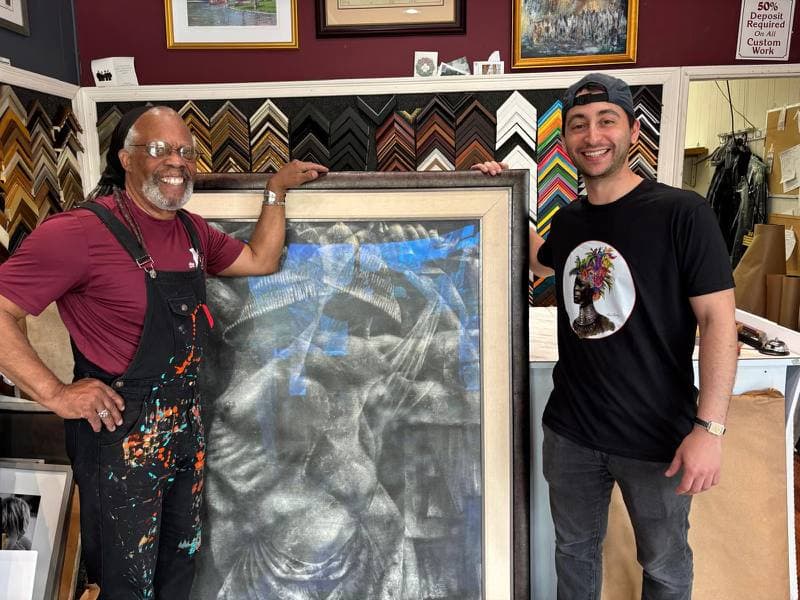 Paul Goodnight in the shop with one of his paintings framed in a wide silver-leaf moulding