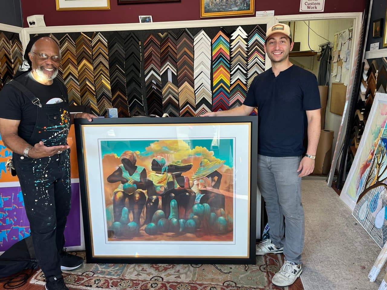 Paul Goodnight at West Roxbury Framing with one of his signed prints of figures in wide-brimmed hats, framed in a black moulding with a gold fillet and white mat